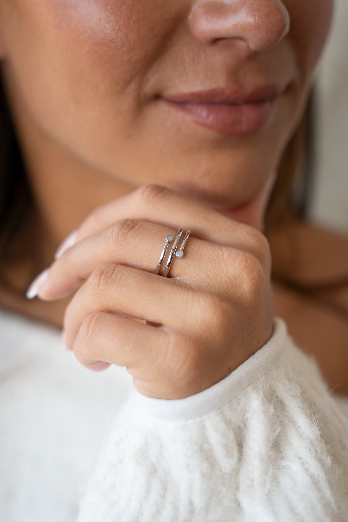Hand unter dem Kinn einer Frau, am Finger der silberne Aurore Spiralring mit zwei kleinen Muttermilchsteinchen