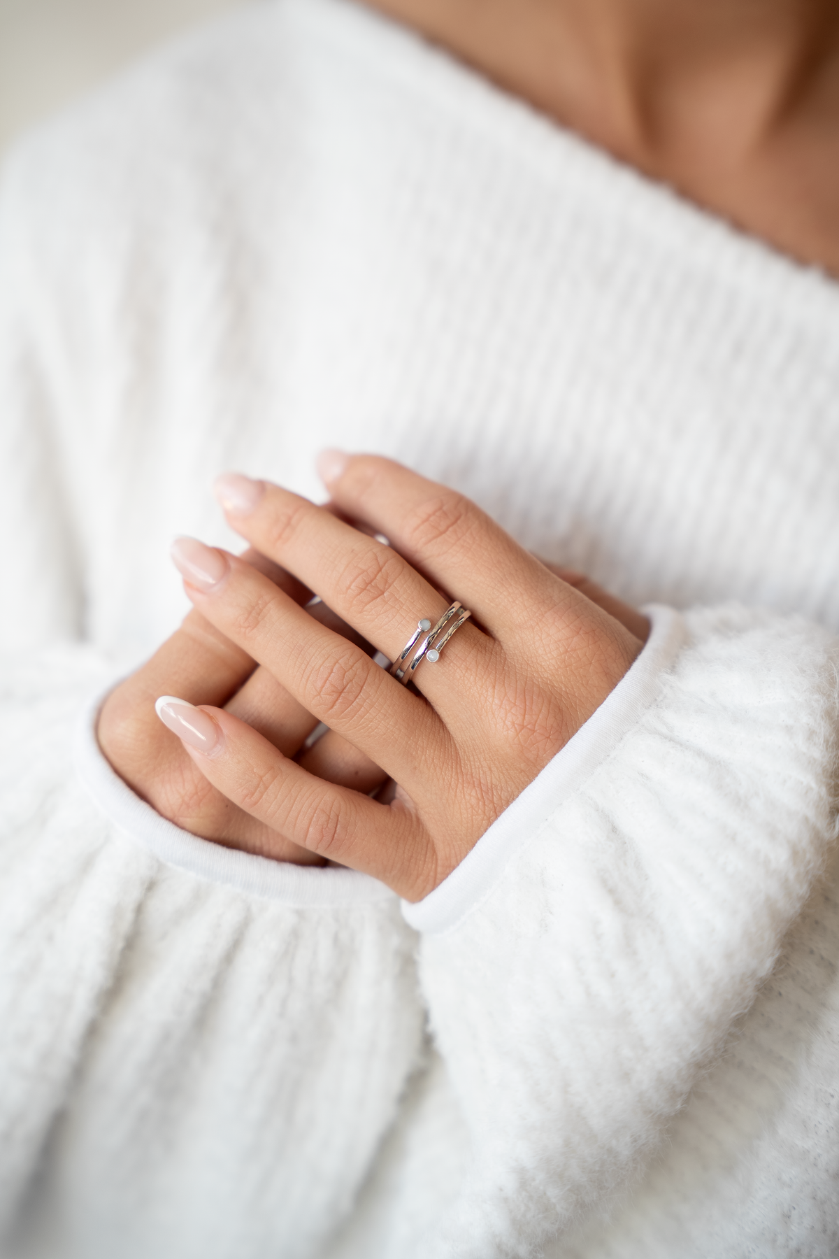 Übereinandergelegte Hände auf weißem Pullover, am Ringfinger der silberne Aurore Muttermilchring