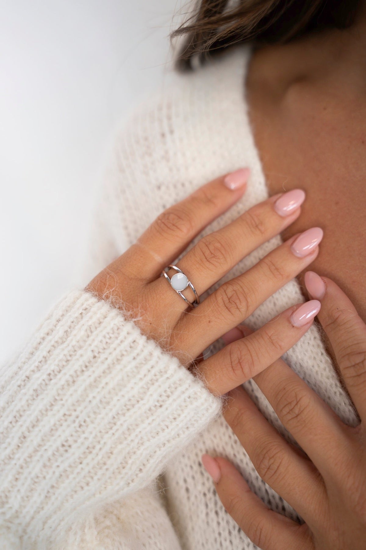 Nahaufnahme des Bea-Rings aus 925er Silber mit rundem Muttermilchstein, die Hand ruht auf einem weißen Strickpullover.