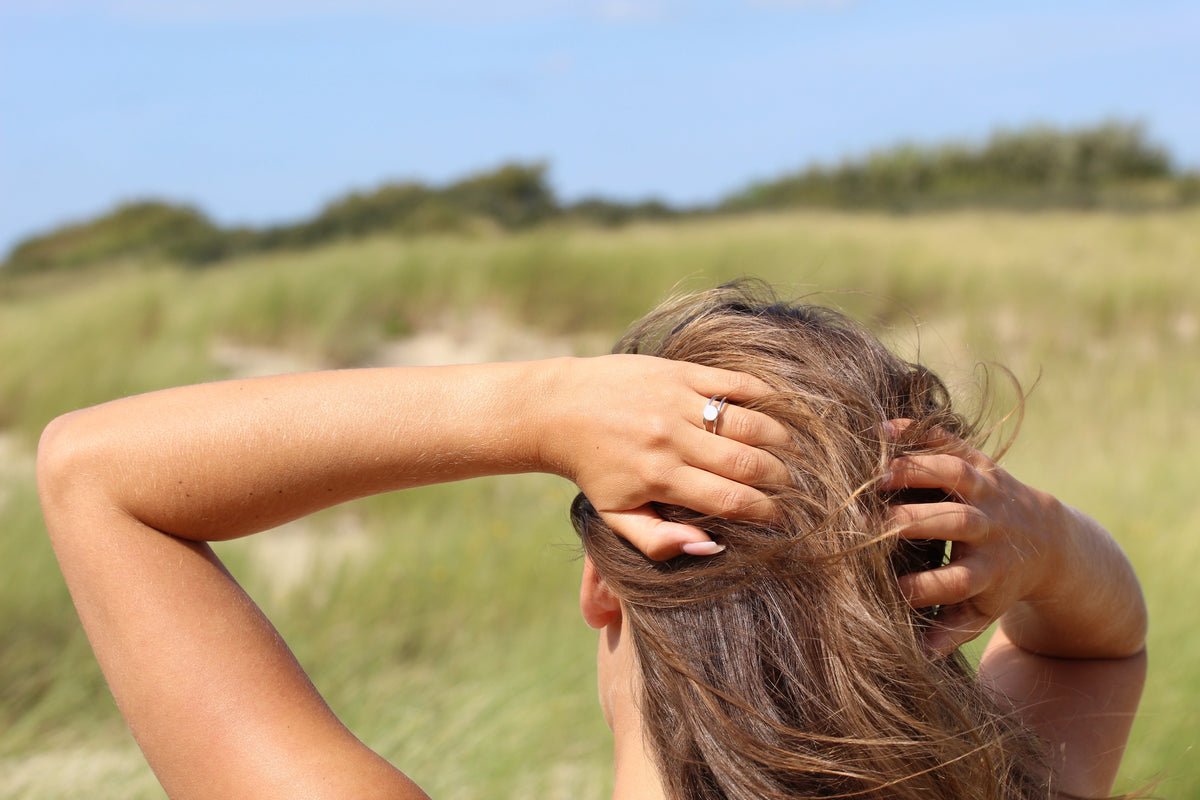 Frau von hinten in den Dünen, Hände im Haar, am Finger der silberne Bea Muttermilchring