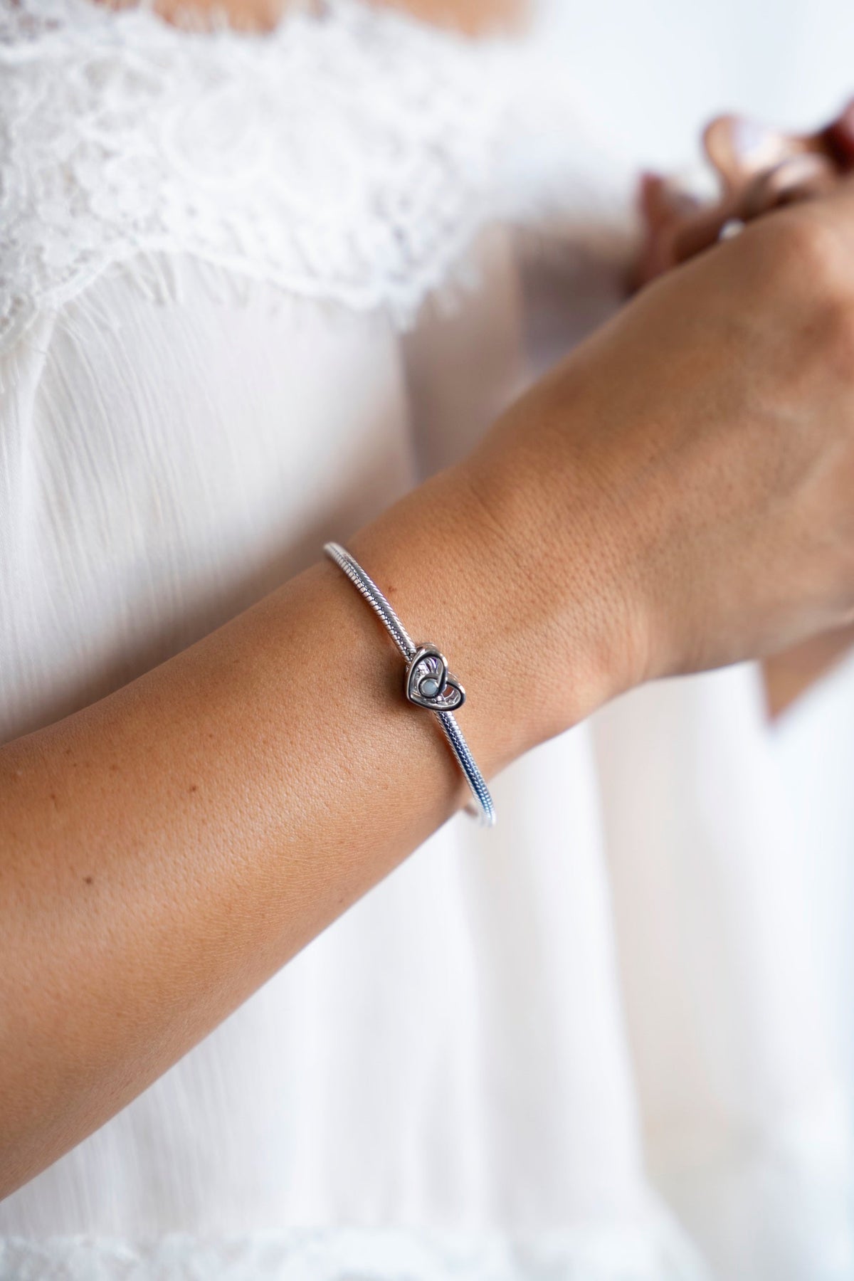 Silberner Bente-Charm in Herzform mit Muttermilch, an einem Charm-Armband am Handgelenk.