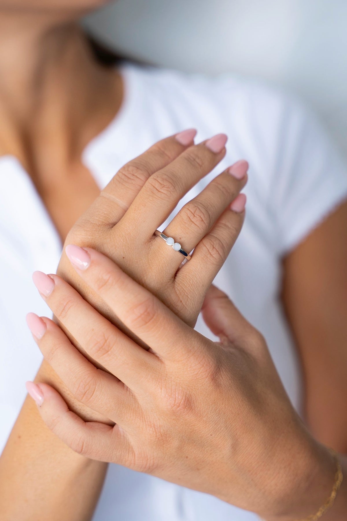 Muttermilchring Bo aus 925er Silber an einer Hand, die auf der anderen Hand ruht, vor einem weißen Shirt.