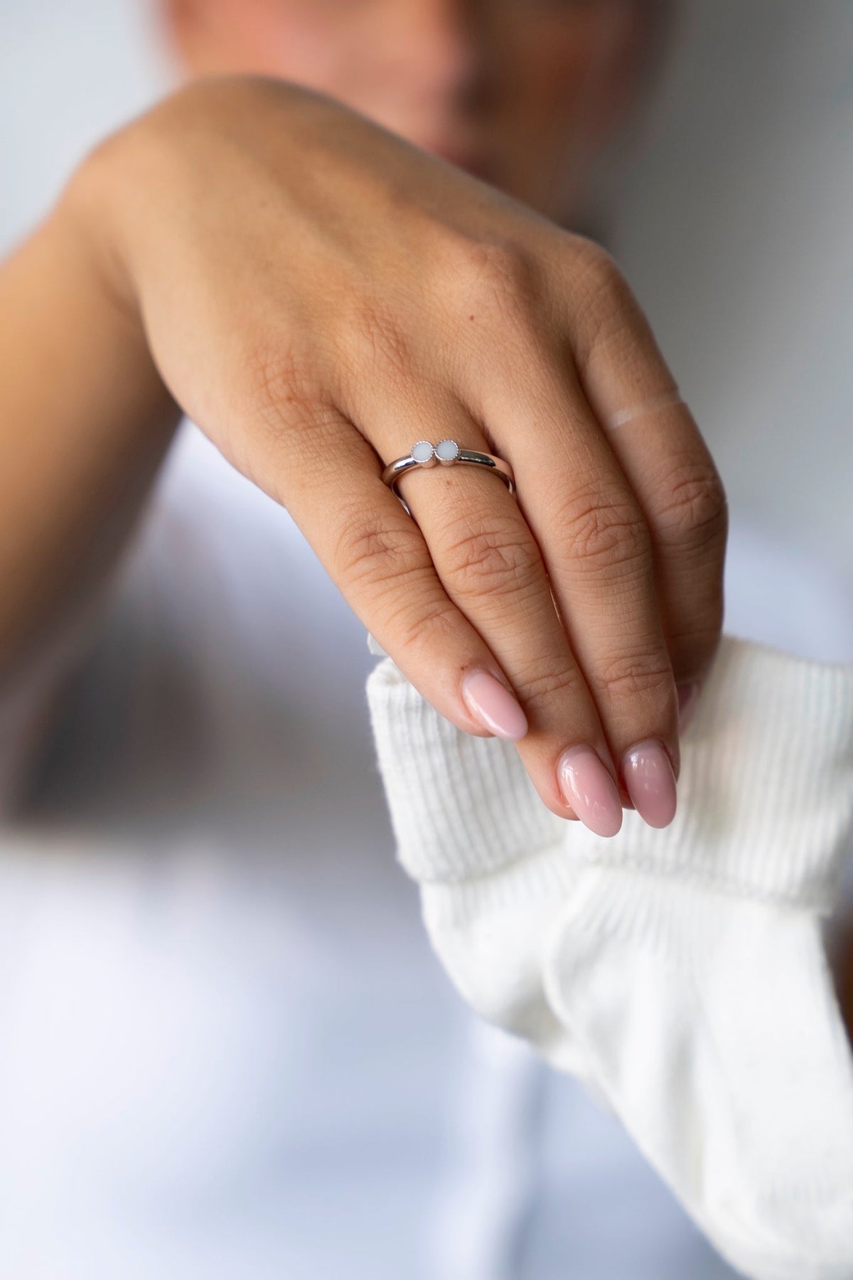 Hand mit dem silbernen Bo-Muttermilchring, die eine weiße Babysocke hält.