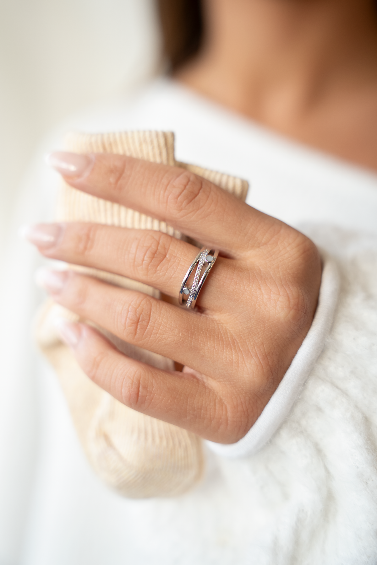 Hand hält ein beiges Babysöckchen, am Ringfinger der Charlotte Muttermilchring mit schräger Reihe klarer Steinchen