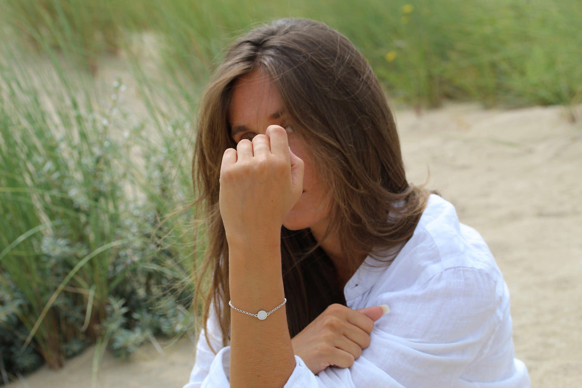 Frau in weißer Bluse am Strand trägt das Armband Circle of Life mit rundem Muttermilchstein am Handgelenk.