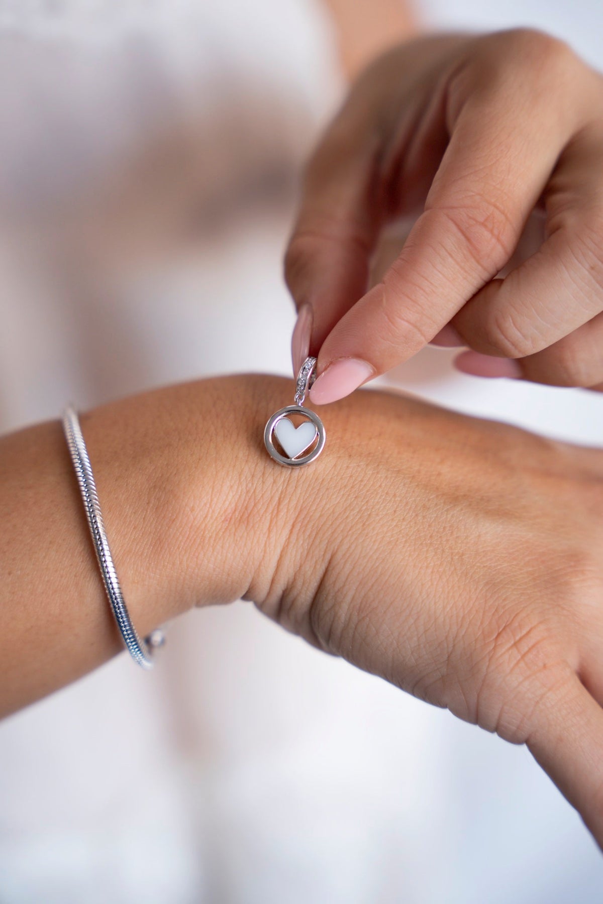 Eline-Muttermilch-Charm aus massivem Weißgold mit herzförmiger Muttermilch in einem runden Rahmen, neben einem Armband.