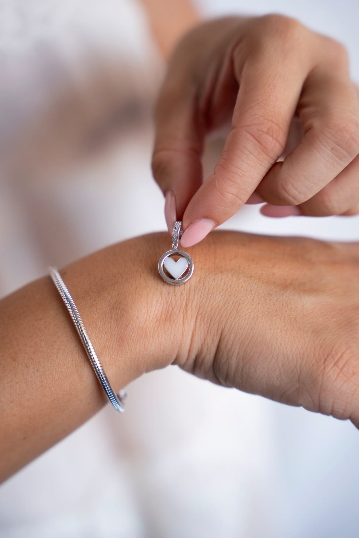 Finger halten den runden weißgoldenen Eline-Charm mit Muttermilchherz über der Hand.