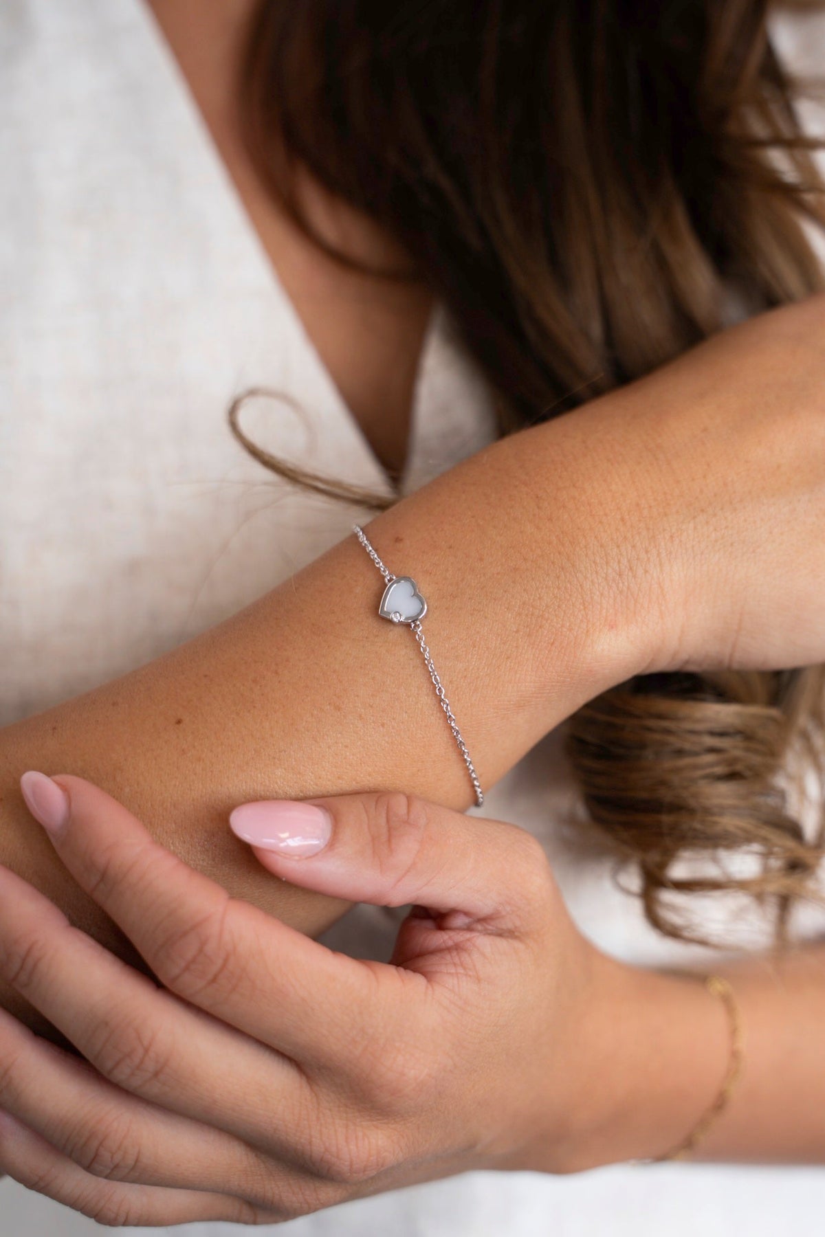 Esmée-Armband aus massivem Weißgold mit Muttermilchherz, am Handgelenk vor einem Leinentop getragen.