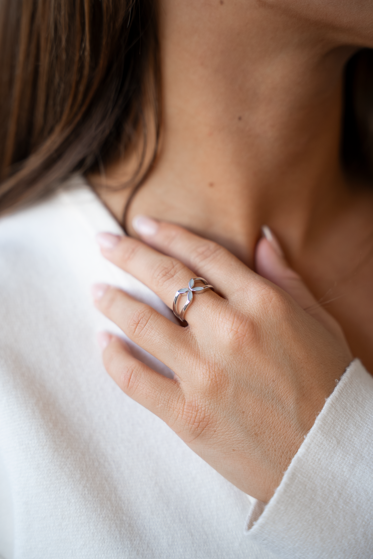 Hand am Hals einer Frau im weißen Pullover, am Ringfinger der Fleur Muttermilchring mit vier Blättern