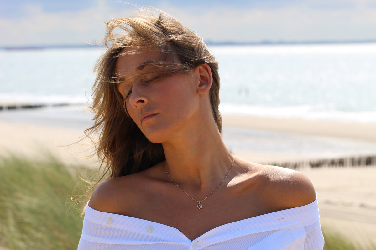 Frau mit geschlossenen Augen am Meer trägt den Heart to Heart Muttermilch-Anhänger an feiner Kette.