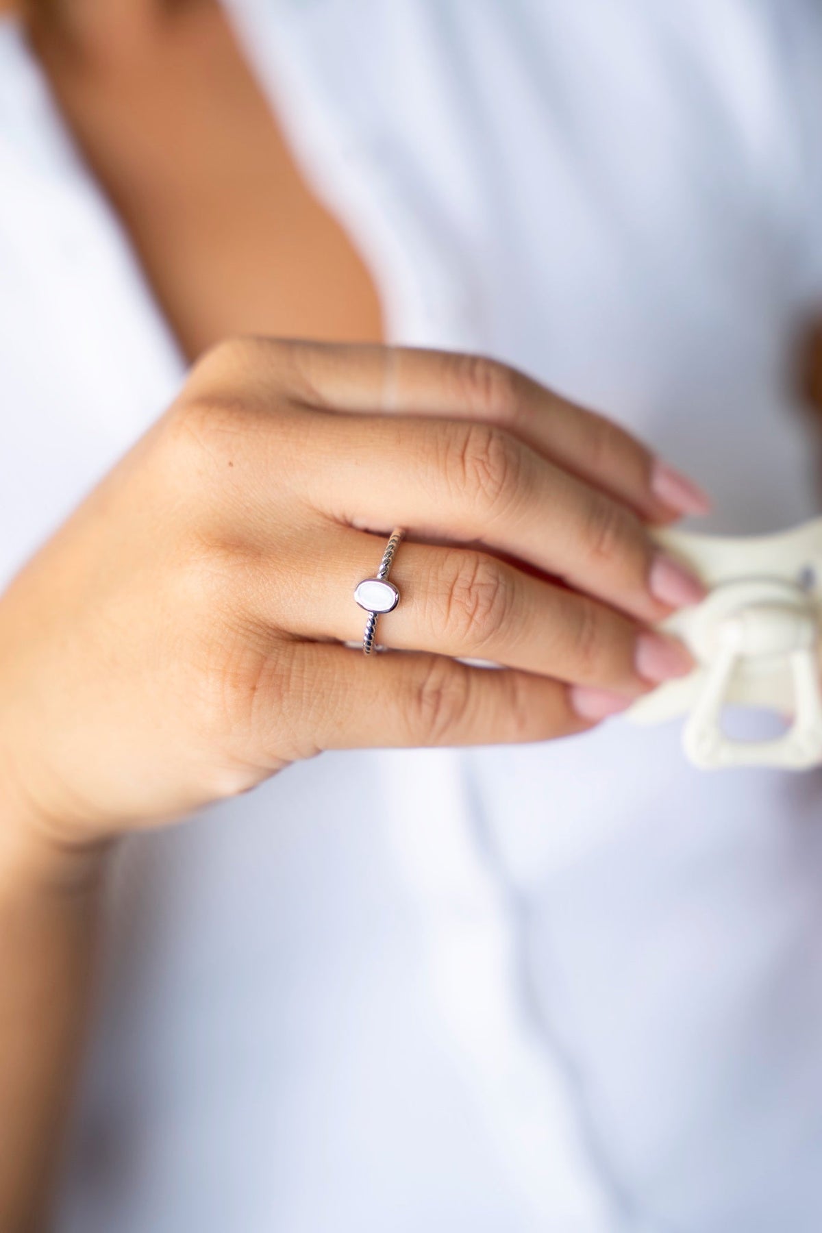 Silberner Ilse-Ring mit ovalem Muttermilchstein und verzierter Ringschiene, mit einem Schnuller in der Hand.
