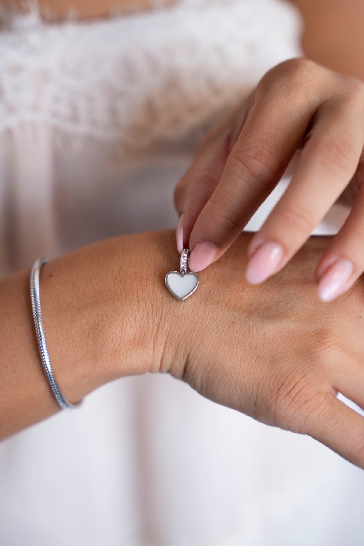 Indy-Muttermilch-Charm aus Silber über der Hand gehalten, neben einem silbernen Armband.