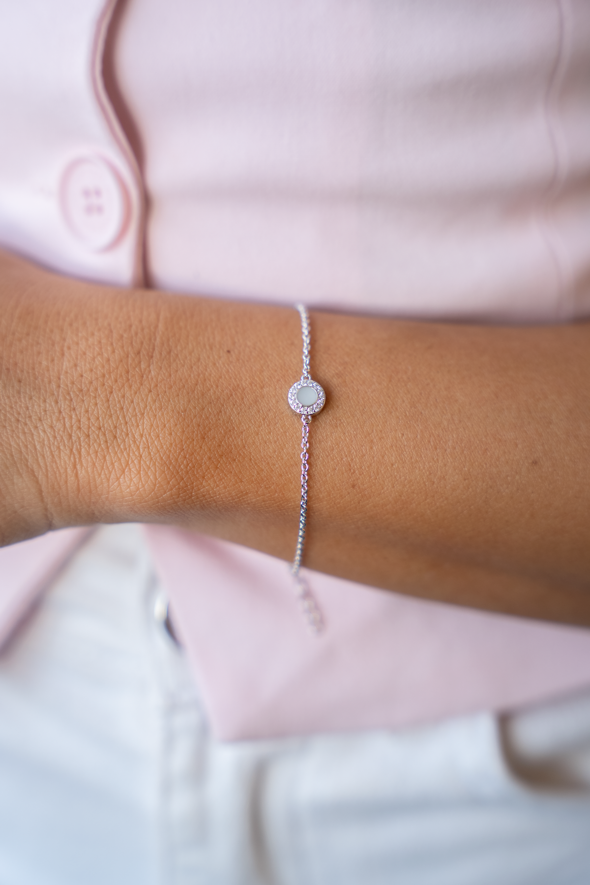 Nahaufnahme des Armbands Juul am Handgelenk: runder Muttermilchstein mit Kranz aus klaren Steinchen an feiner Kette.