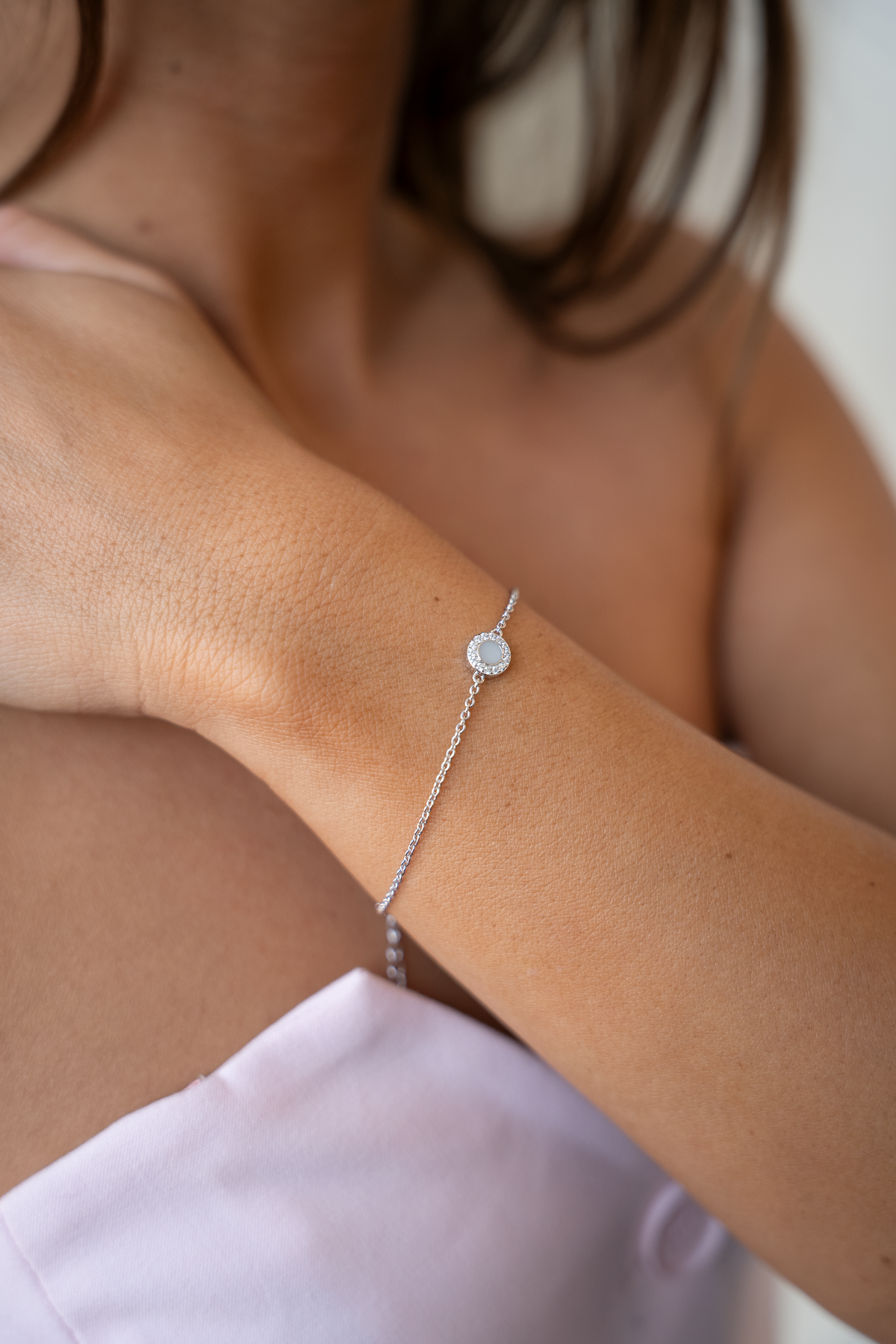 Armband Juul mit rundem Muttermilchstein und Steinchenkranz am Handgelenk einer Frau, die die Hand an die Schulter legt.