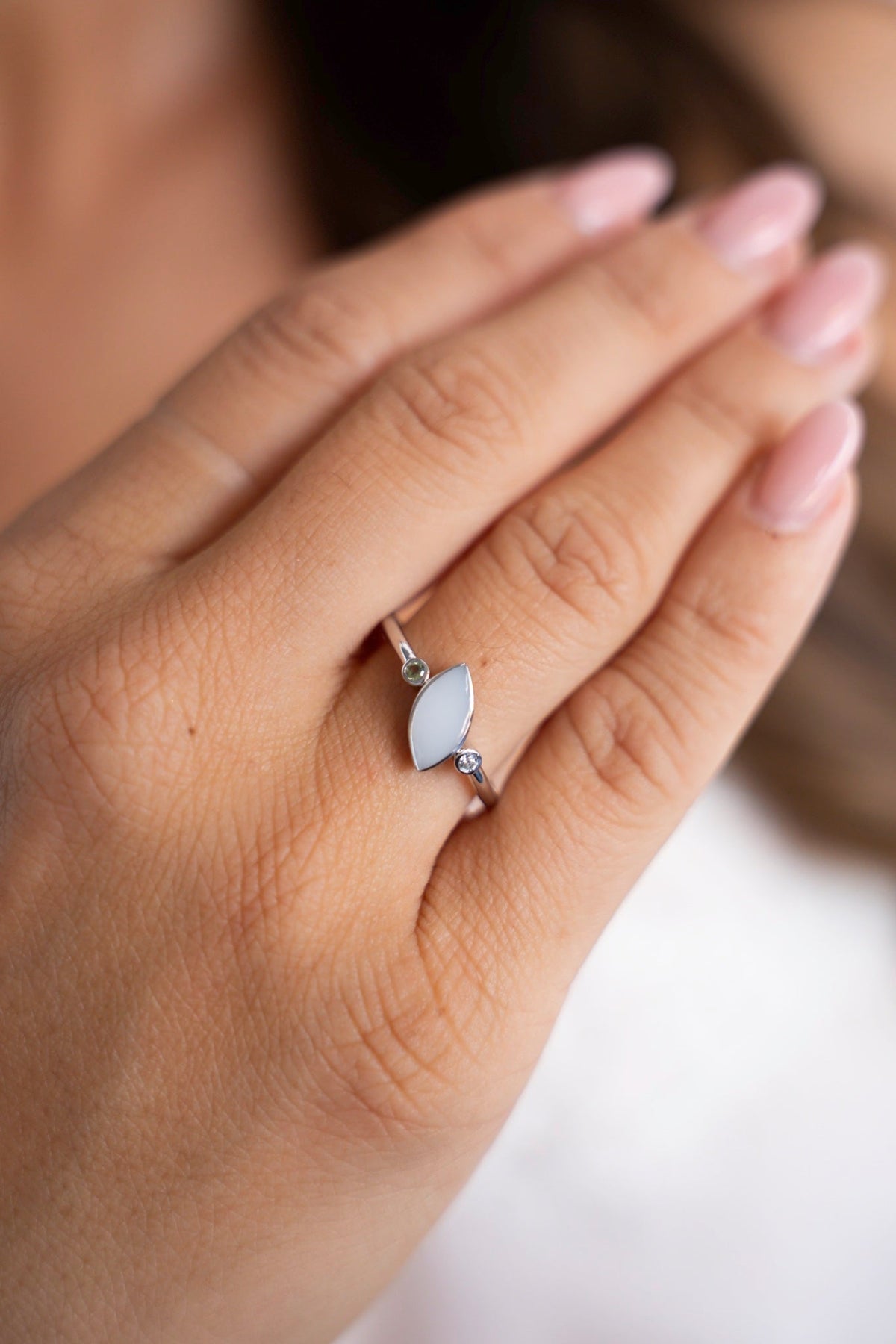 Nahaufnahme des silbernen Lina-Duo-Rings: ein ovaler Muttermilchstein zwischen zwei kleinen Geburtssteinen, an der Hand getragen.