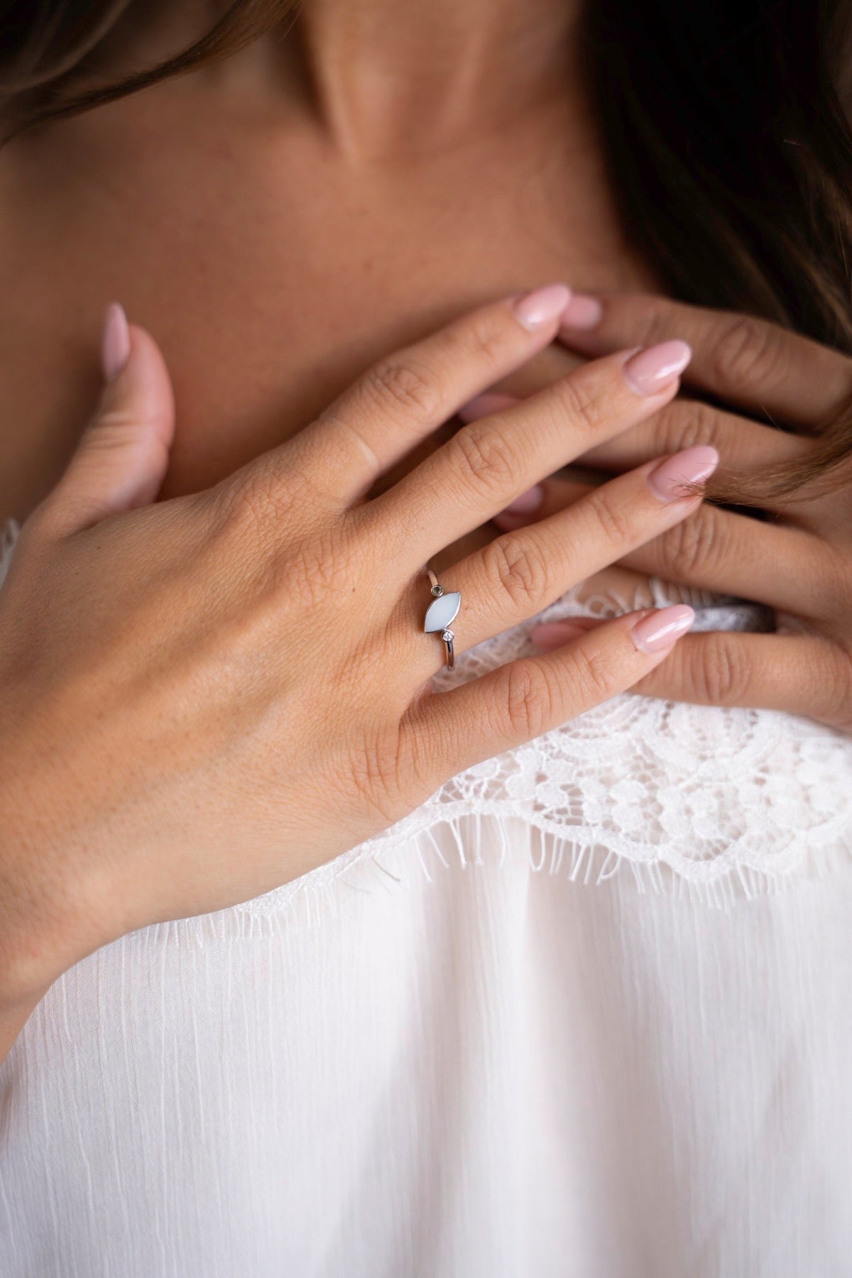 Hände auf der Brust mit dem silbernen Lina-Duo-Ring, ein Muttermilchstein mit zwei kleinen Steinchen, vor einem weißen Spitzentop.