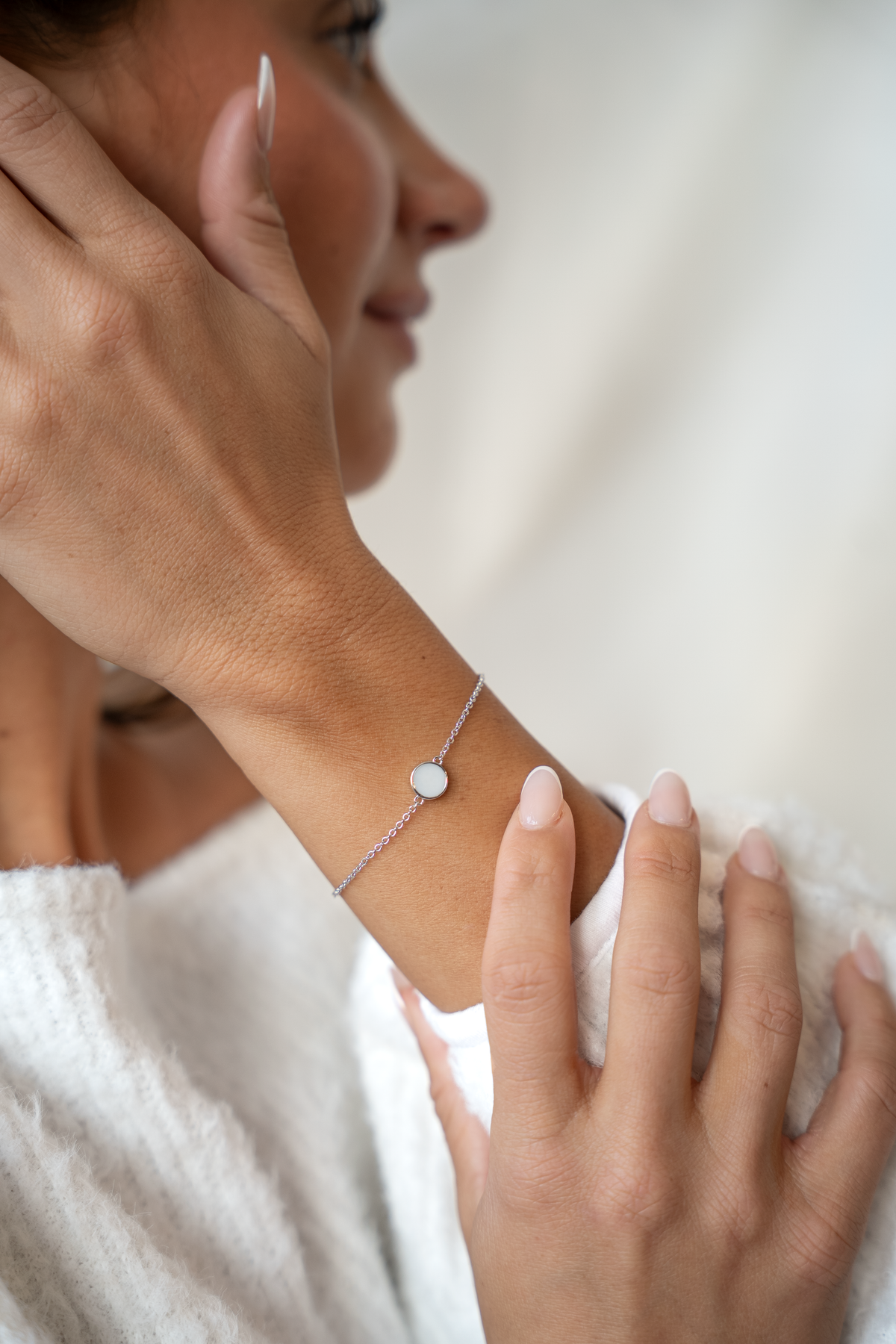 Silbernes Armband Lis mit flachem rundem Muttermilchstein am Handgelenk einer Frau, die ihre Hand an die Wange legt.
