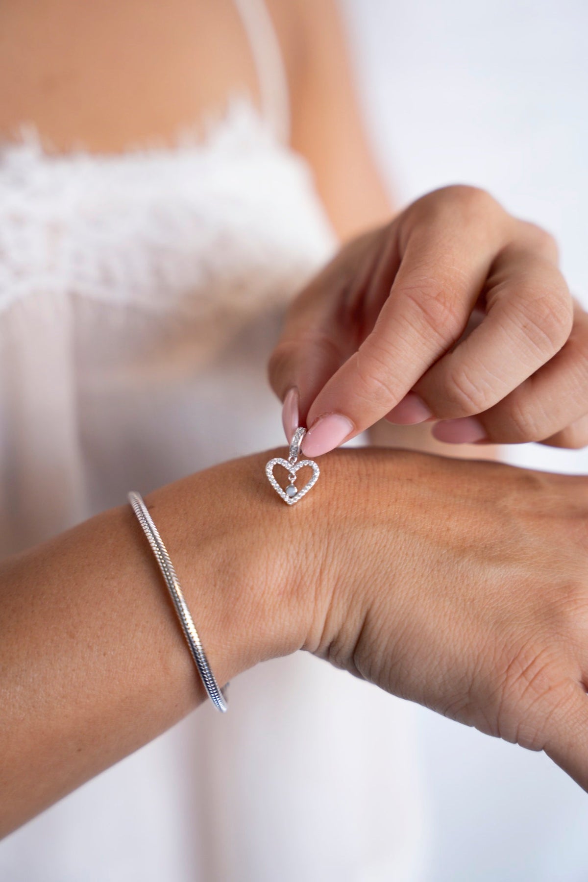 Sophie-Herzcharm aus Silber mit Muttermilch, neben einem Armband am Handgelenk.